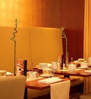 Un comedor con mesas de madera, sillas blancas y un banco acolchado amarillo.