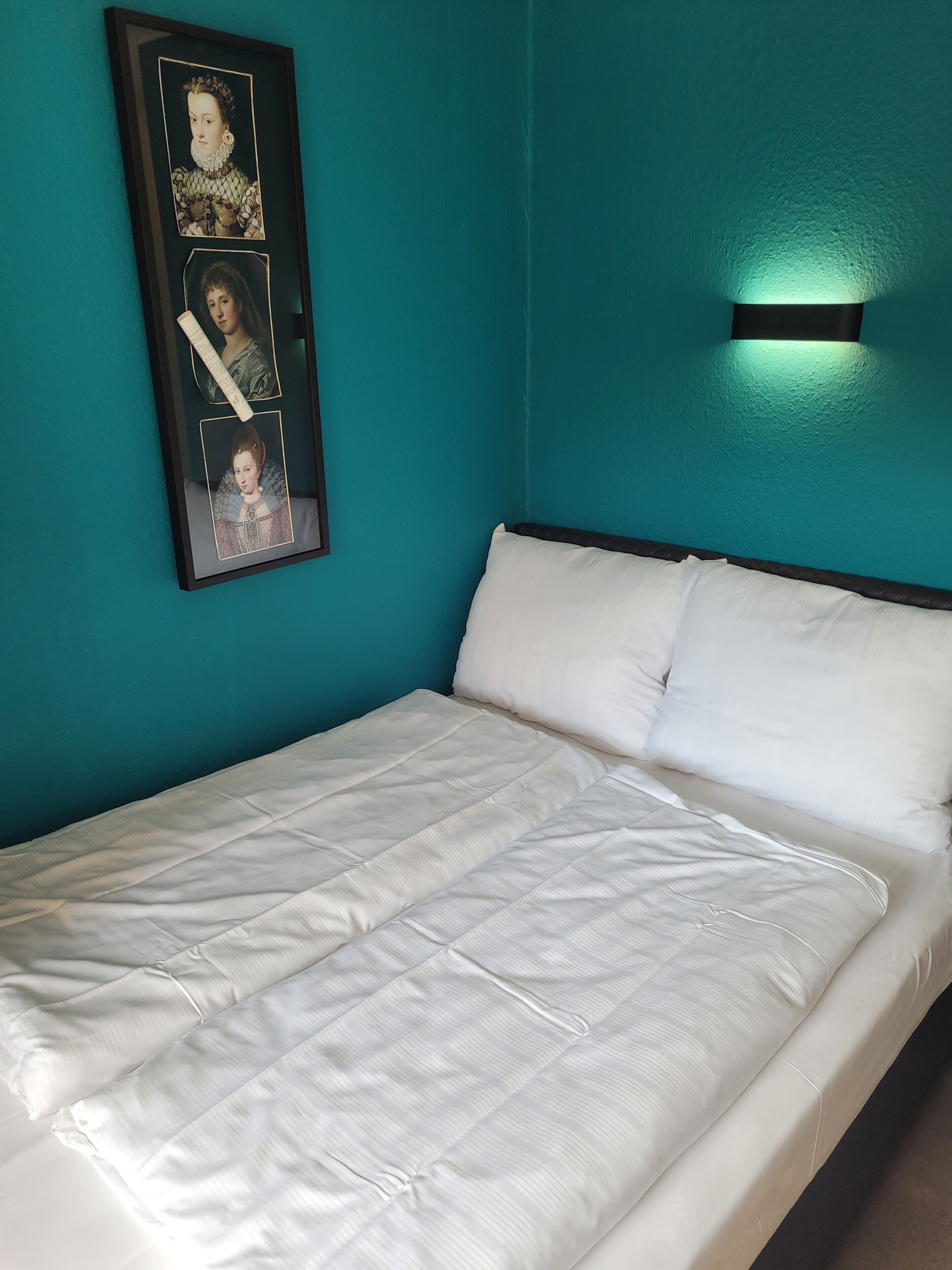 Ein ordentlich bezogenes Bett mit weißer Bettwäsche in einem Zimmer mit türkisblauen Wänden.