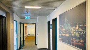 A hotel corridor with a view of a cityscape at night, a carpeted floor, and doors leading to rooms. - Hotel Christina (Cologne)