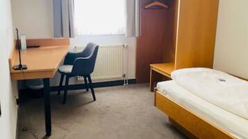 Ein kompaktes Hotelzimmer mit einem Einzelbett, einem Schreibtisch mit Stuhl, einem an der Wand befestigten Fernseher und einem Kleiderschrank.