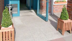 An open blue door leading into a building, with a trash bin and two potted plants on the ground. - Hotel Christina (Cologne)