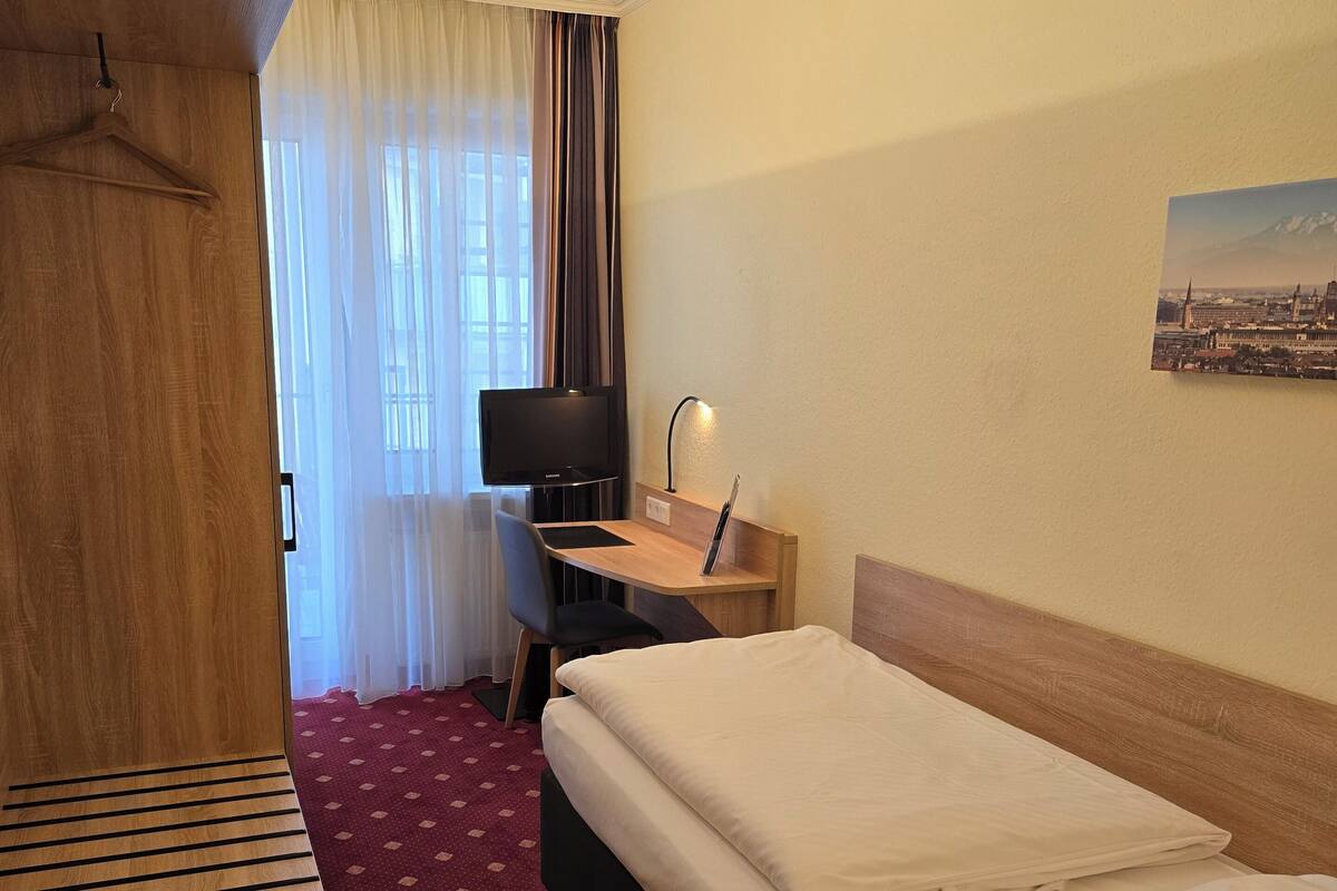Habitación de hotel con cama, escritorio con computadora, televisión y armario.