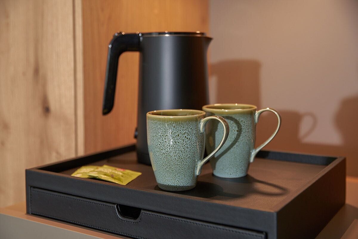 Un vassoio con due tazze di ceramica e un bollitore elettrico nero su un ripiano di legno.