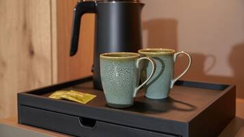 Una bandeja con dos tazas de cerámica y una tetera eléctrica negra sobre una superficie de madera.