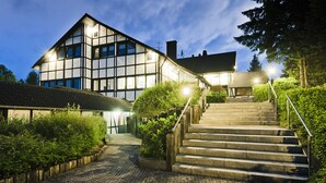 A building with a traditional architectural style, featuring a staircase leading to the entrance. - Sporthotel Grafenwald (Daun)