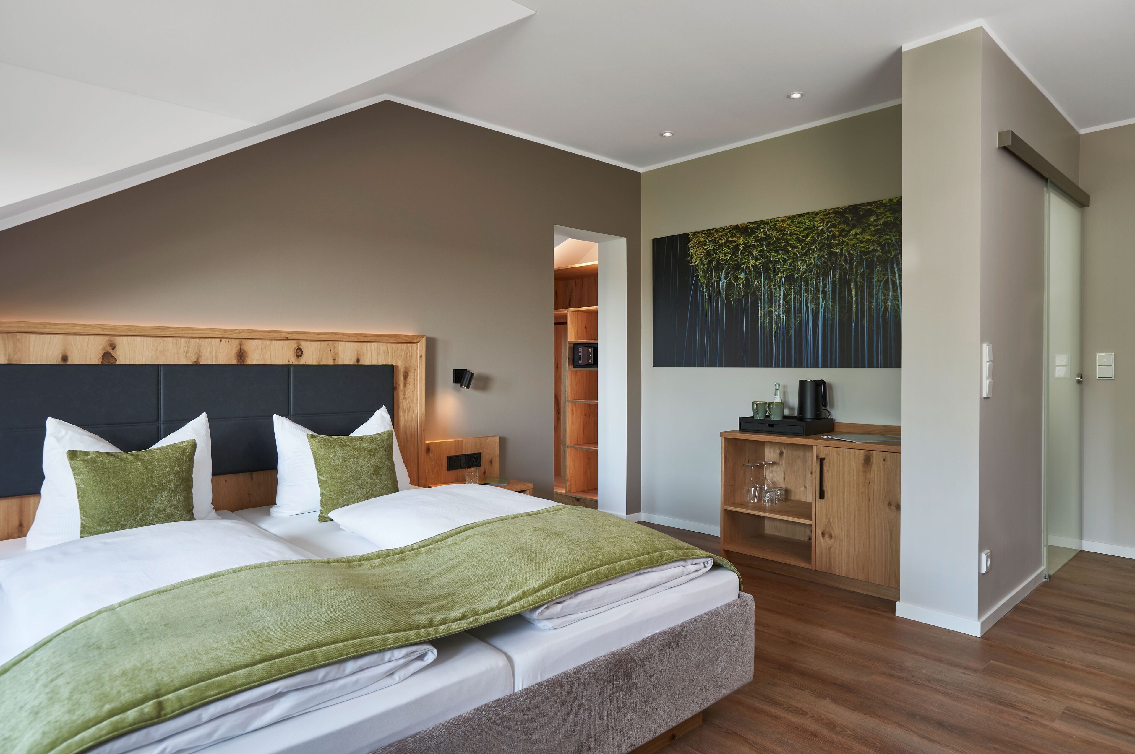 Un dormitorio moderno con una cama grande, un cabecero de madera, una manta verde y un cuadro con árboles en la pared.