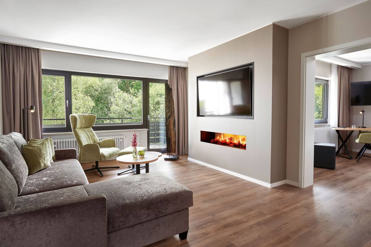 A modern living room with a sofa, a chair, a coffee table, a fireplace, and a TV mounted on the wall.