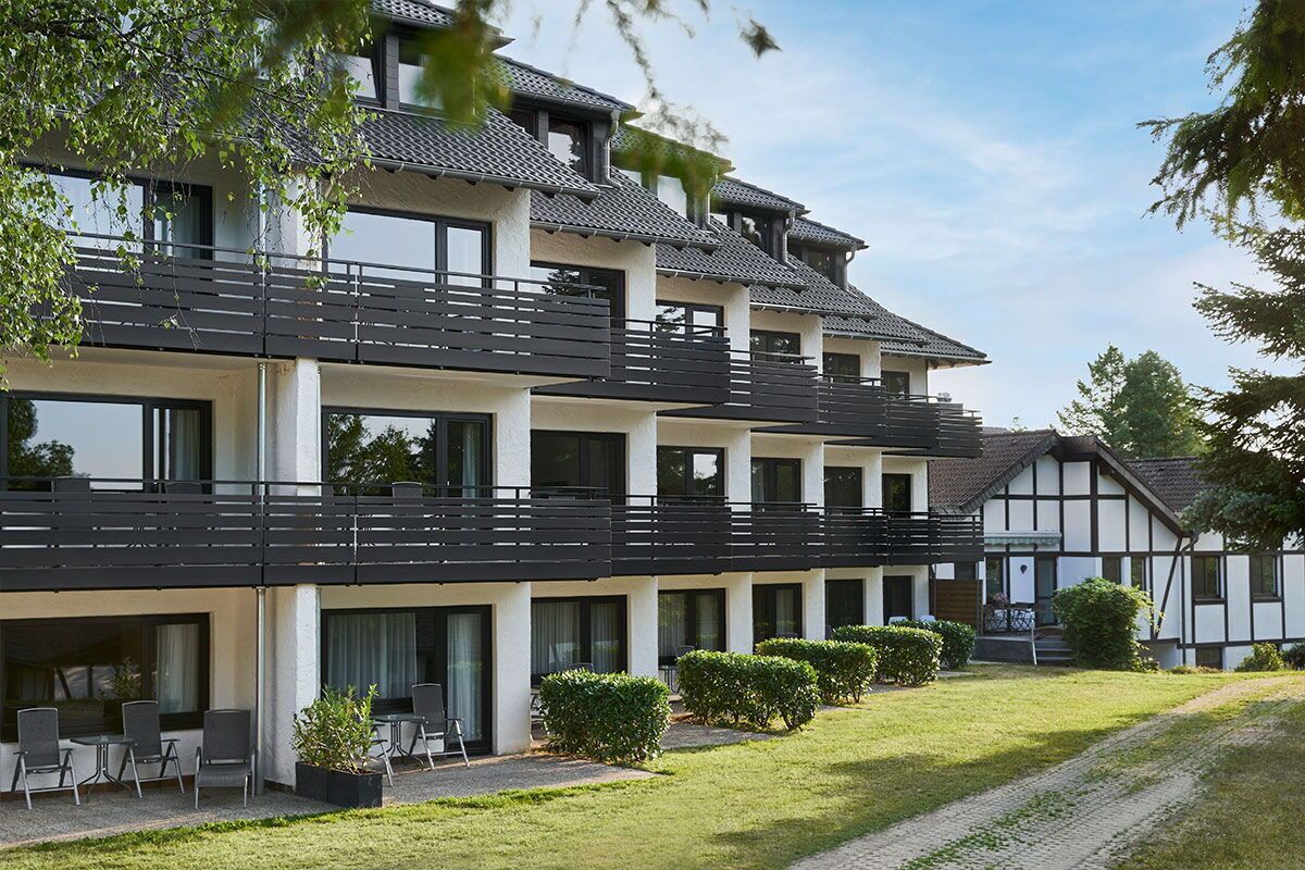 Un hôtel à plusieurs étages, doté d’un design moderne, avec des balcons, de grandes fenêtres et une pelouse bien entretenue.