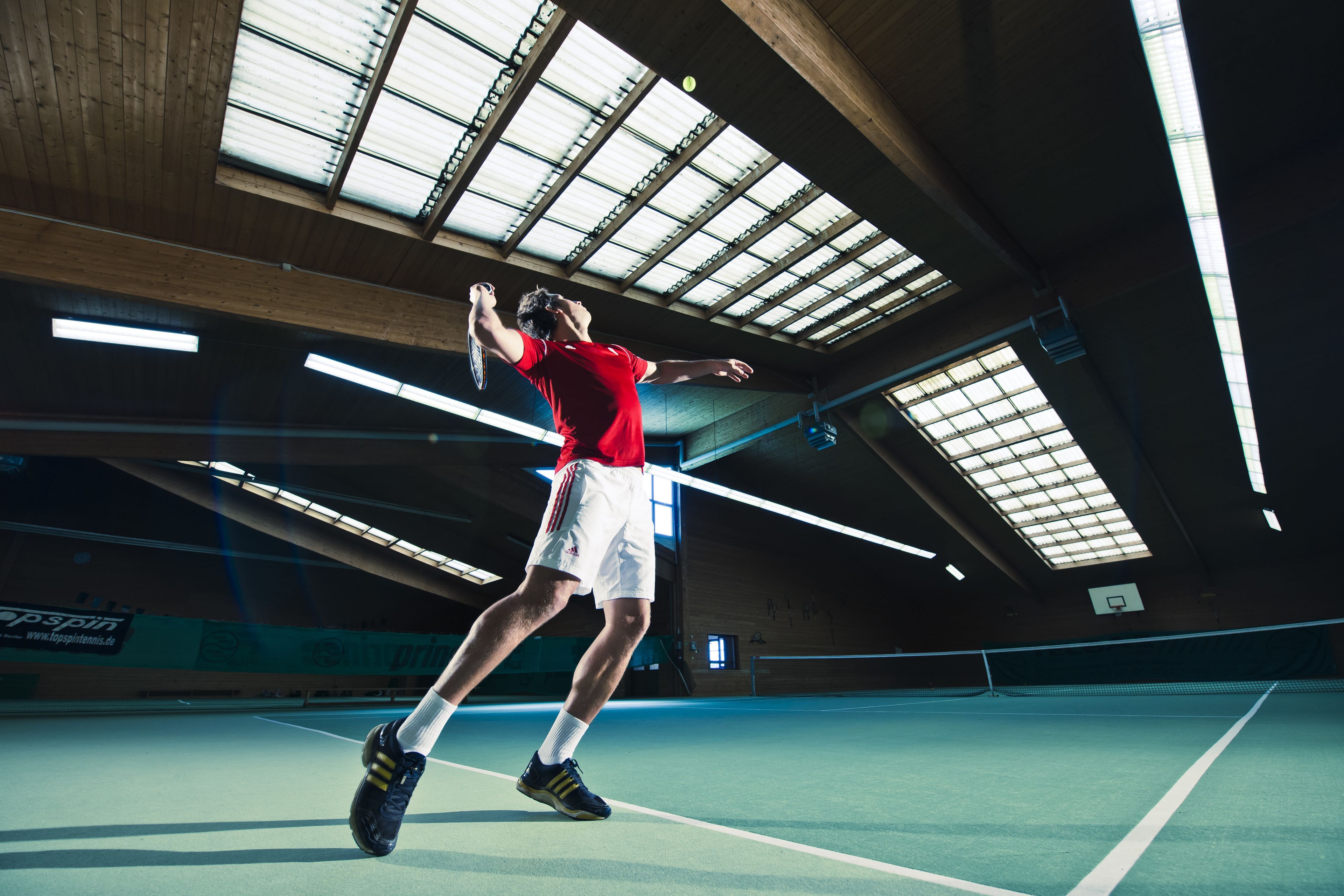 Una cancha de tenis interior con techo alto y tragaluces.