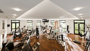 A spacious gym with various exercise equipment, large windows, and a high ceiling. - Sporthotel Grafenwald (Daun)