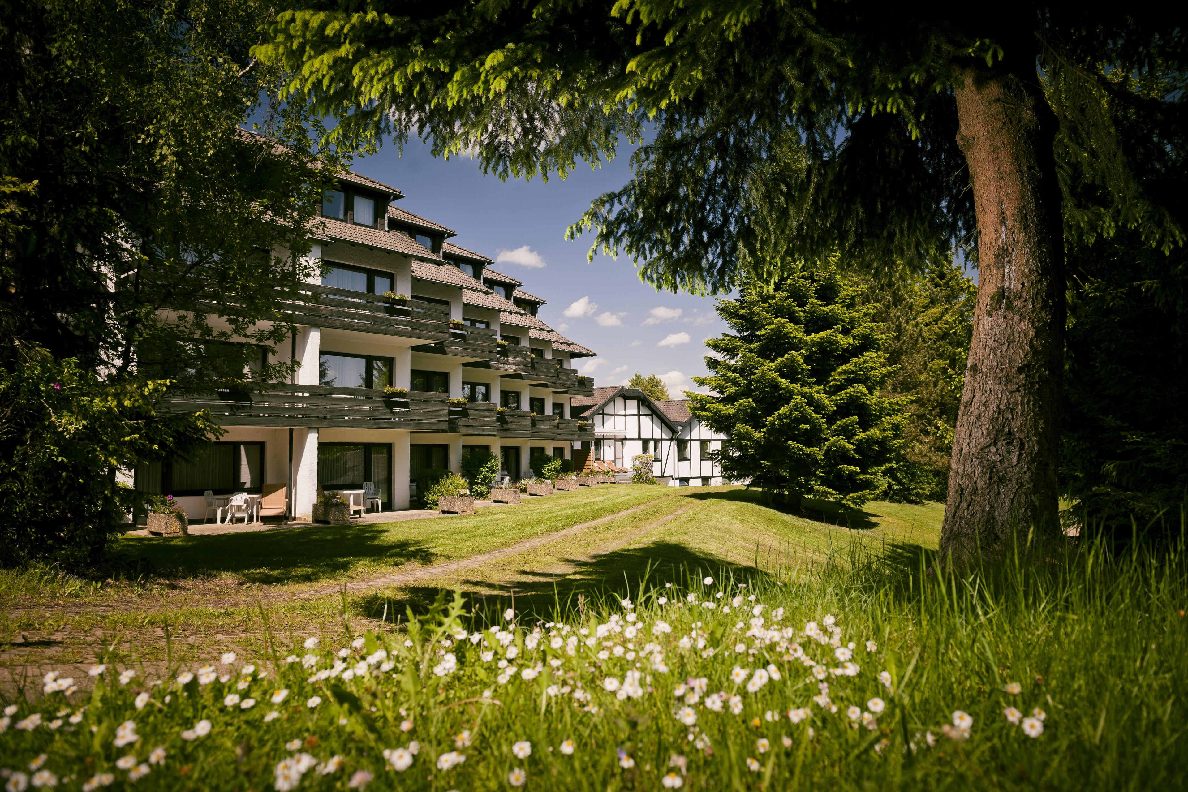 A multi-story building with a garden in front, surrounded by trees.