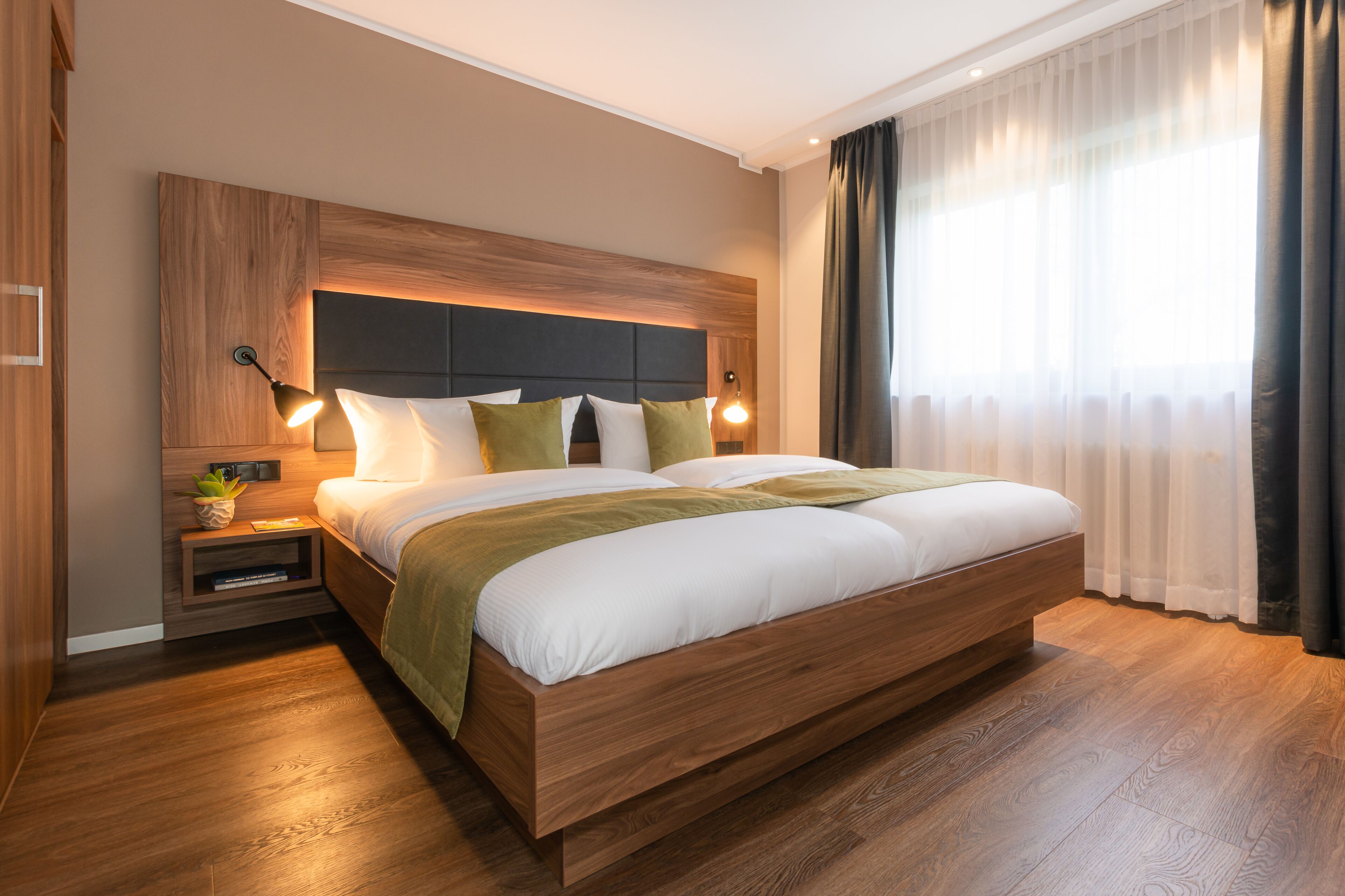 Ein modernes Hotelzimmer mit einem großen Bett, einem Holzkopfstück, Nachttischlampen und einem Nachttisch mit einer Pflanze.