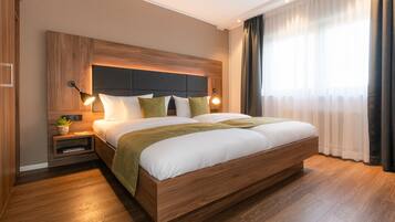 Ein modernes Hotelzimmer mit einem großen Bett, einem Holzkopfstück, Nachttischlampen und einem Nachttisch mit einer Pflanze.