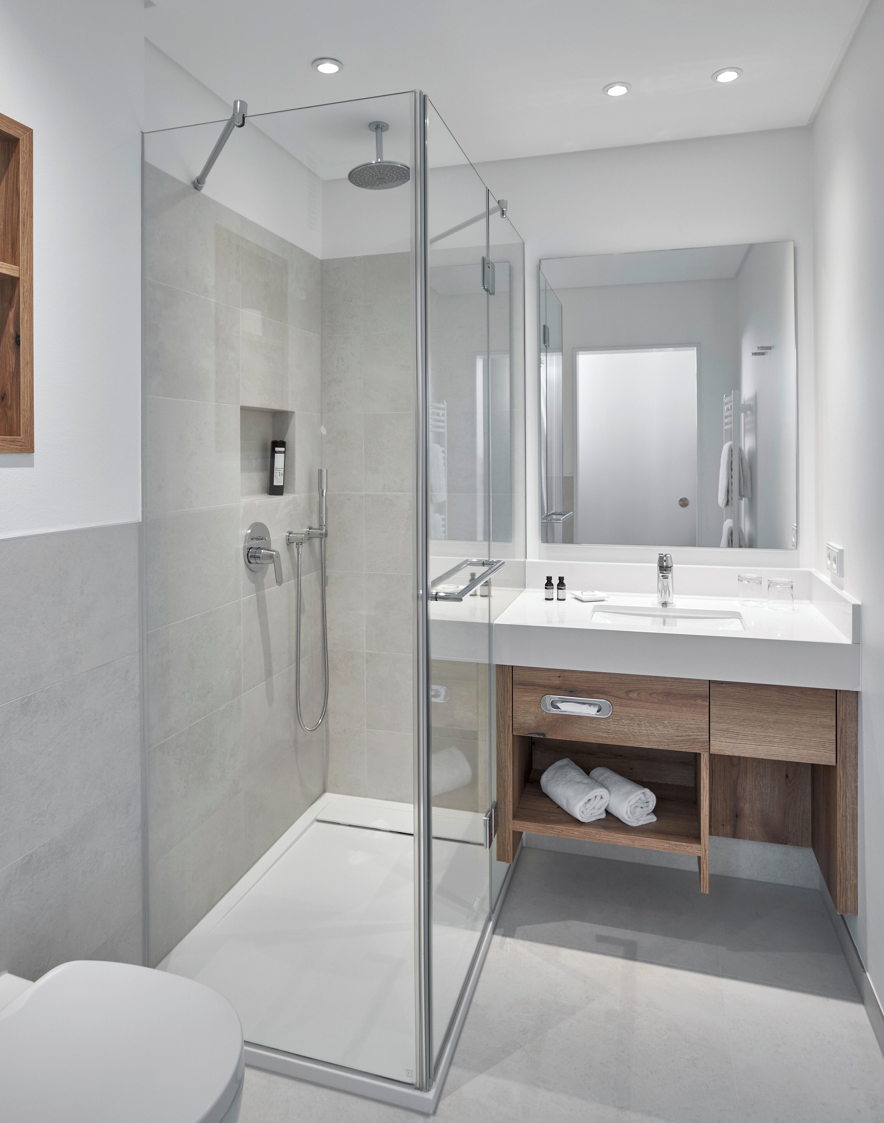 Een moderne badkamer met een douche met glazen wand, een grote spiegel en een houten wastafelmeubel.