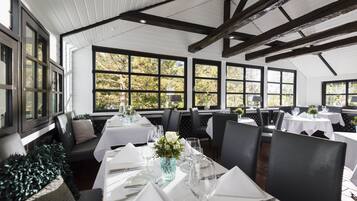 Ein Restaurant mit weißen Tischen, schwarzen Stühlen und großen Fenstern.