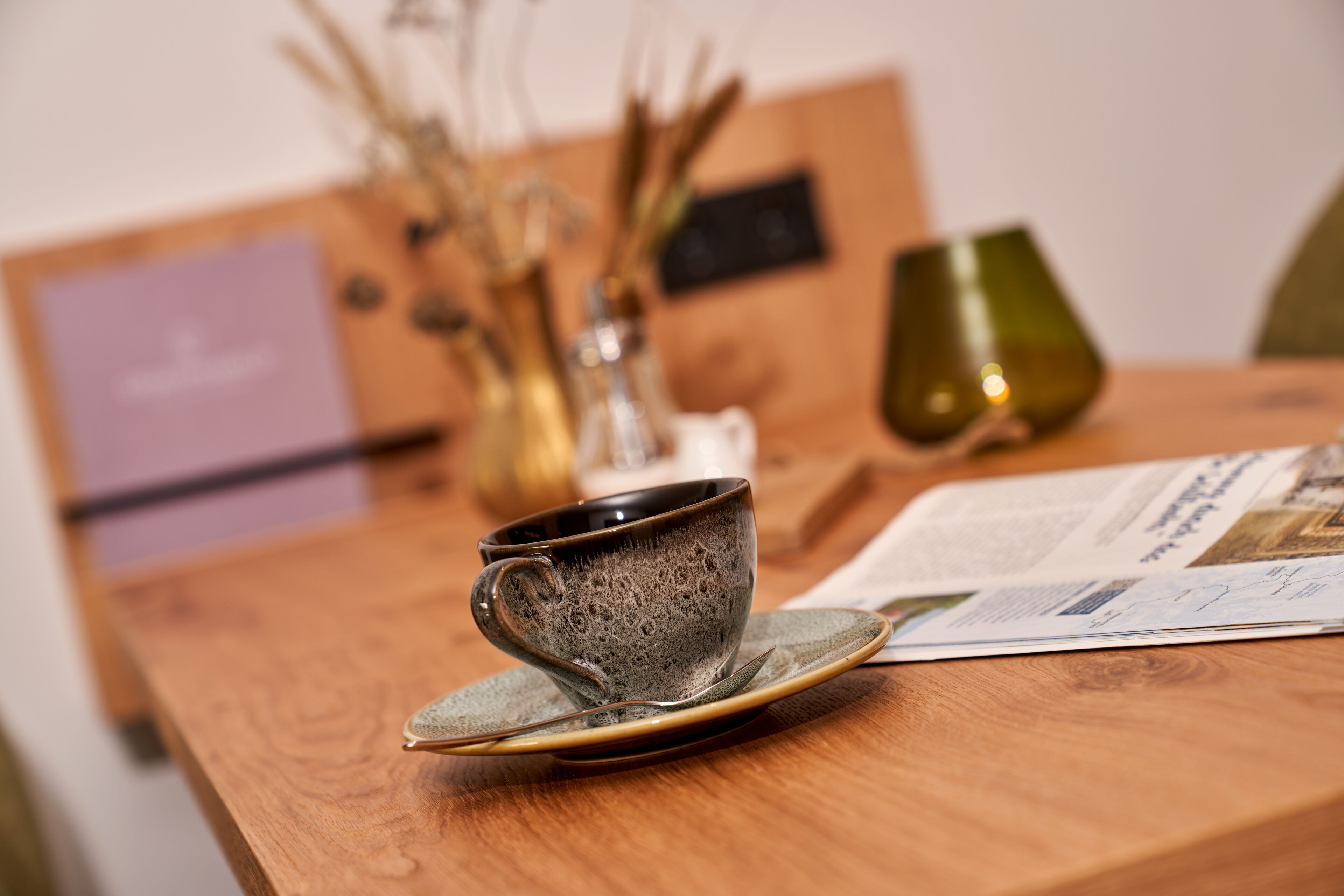 A wooden table with a ceramic cup and saucer, a glass, and a menu.