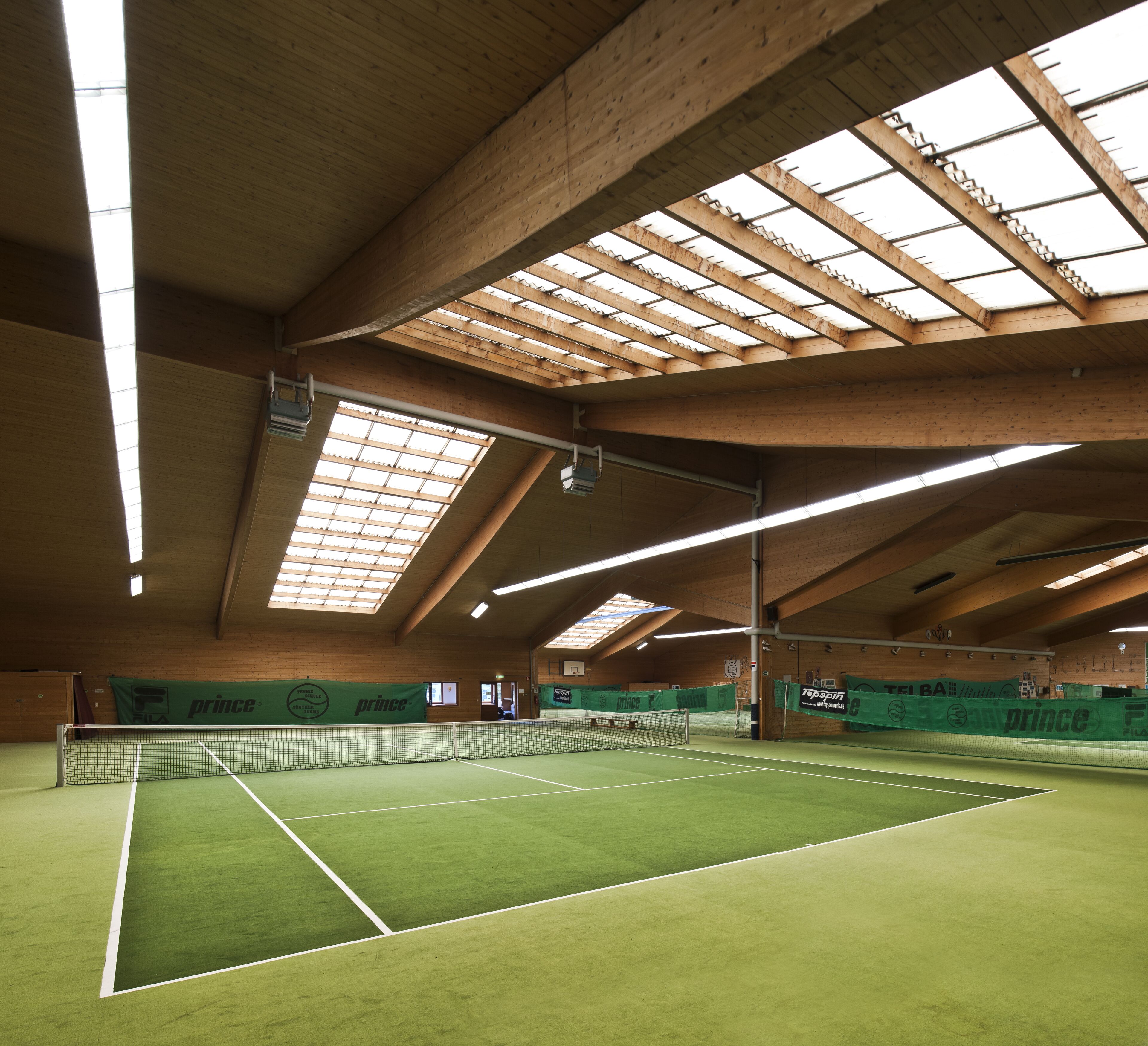 An indoor tennis court with a high ceiling and skylights.