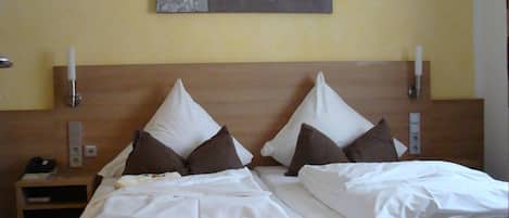 A double bed with white linens, a wooden headboard, and a wall-mounted artwork above.