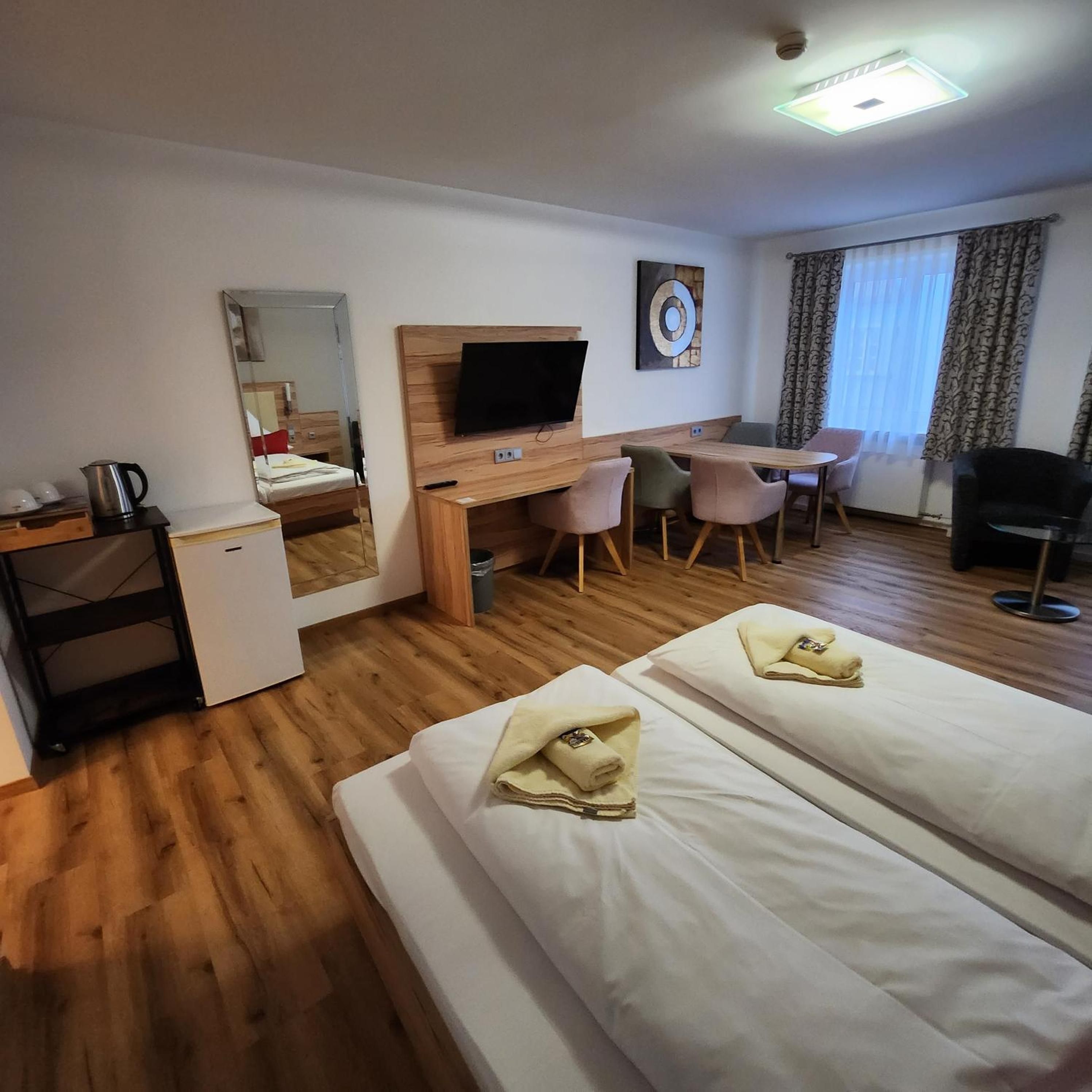 Ein Hotelzimmer mit zwei Betten, einem Schreibtisch, einem Stuhl, einem Fernseher und einem Fenster mit Vorhängen.