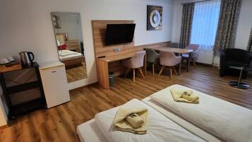 Ein Hotelzimmer mit zwei Betten, einem Schreibtisch, einem Stuhl, einem Fernseher und einem Fenster mit Vorhängen.
