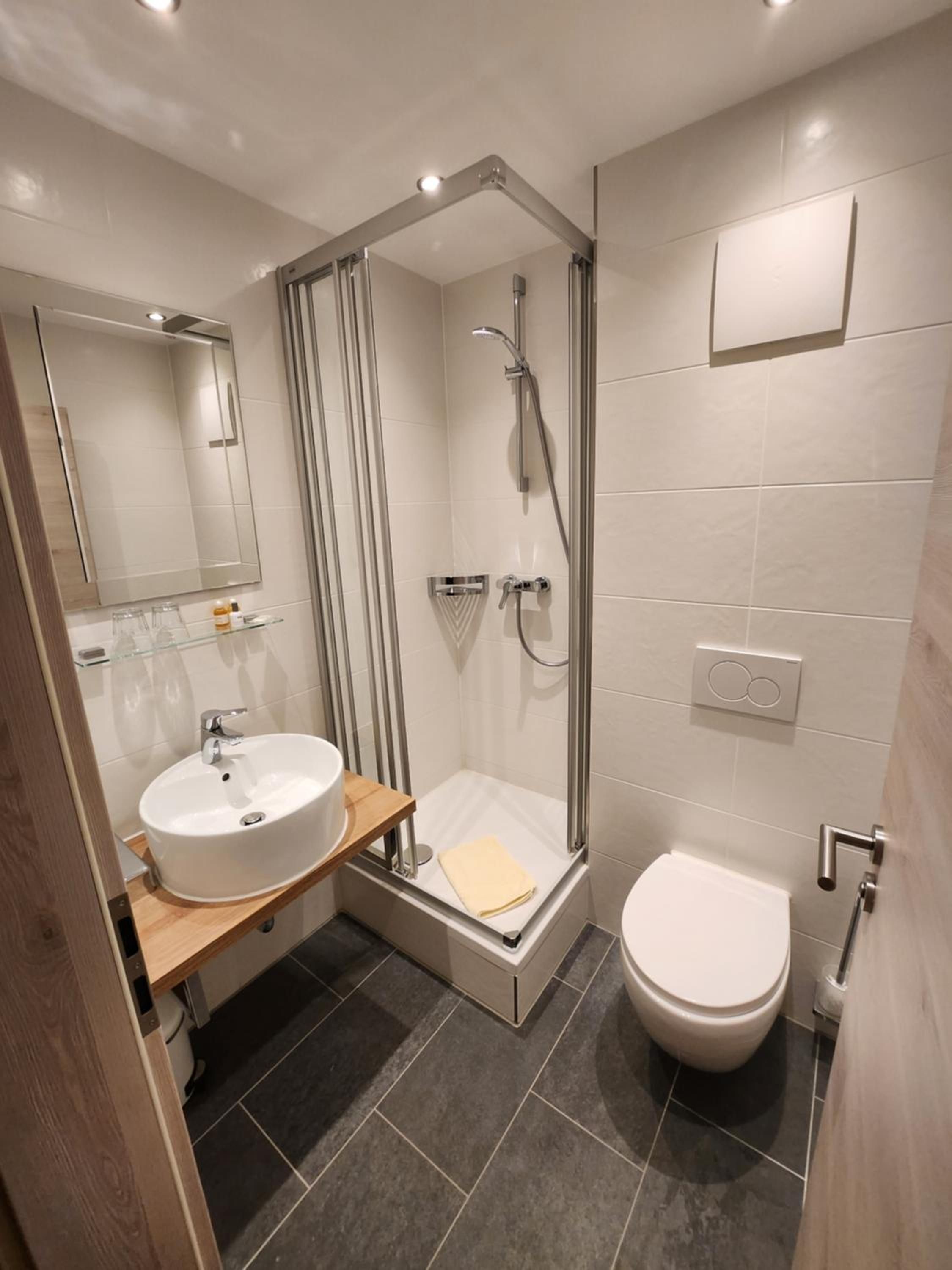 Ein modernes Badezimmer mit einer gläsernen Duschkabine, einem Waschbecken mit Holzablage und einer Toilette.