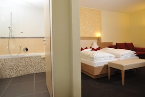 A hotel room with a shower, a bed with red pillows, and a bedside table. - Posthotel Traube (Donauwoerth)