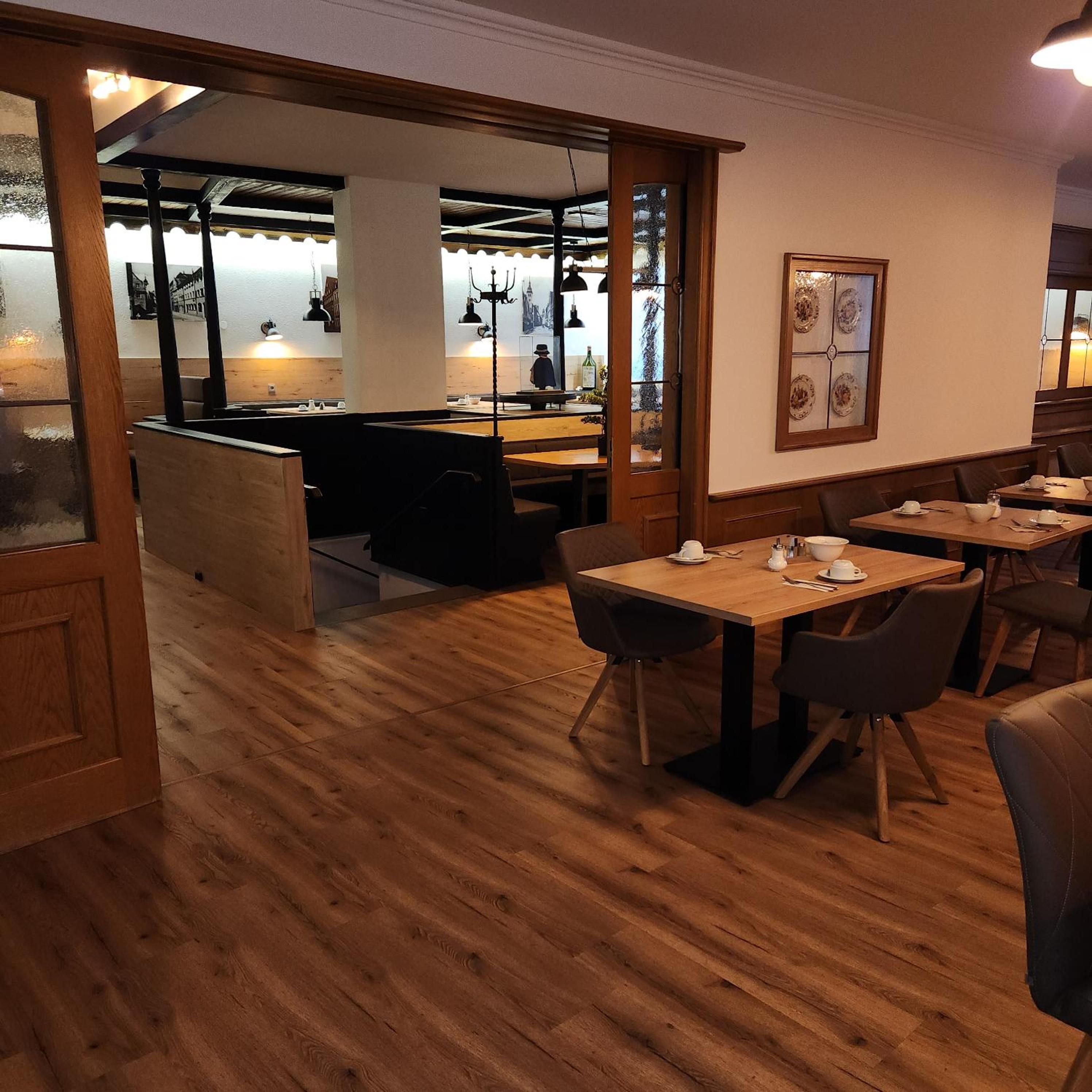 Ein Restaurant mit Holzboden, Tischen, Stühlen und einer Bar mit hängenden Lampen.