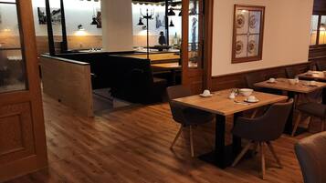 Ein Restaurant mit Holzboden, Tischen, Stühlen und einer Bar mit hängenden Lampen.