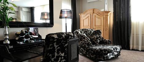 A room with a black and white patterned armchair, a wooden cabinet, a desk with a mirror, and a potted plant.