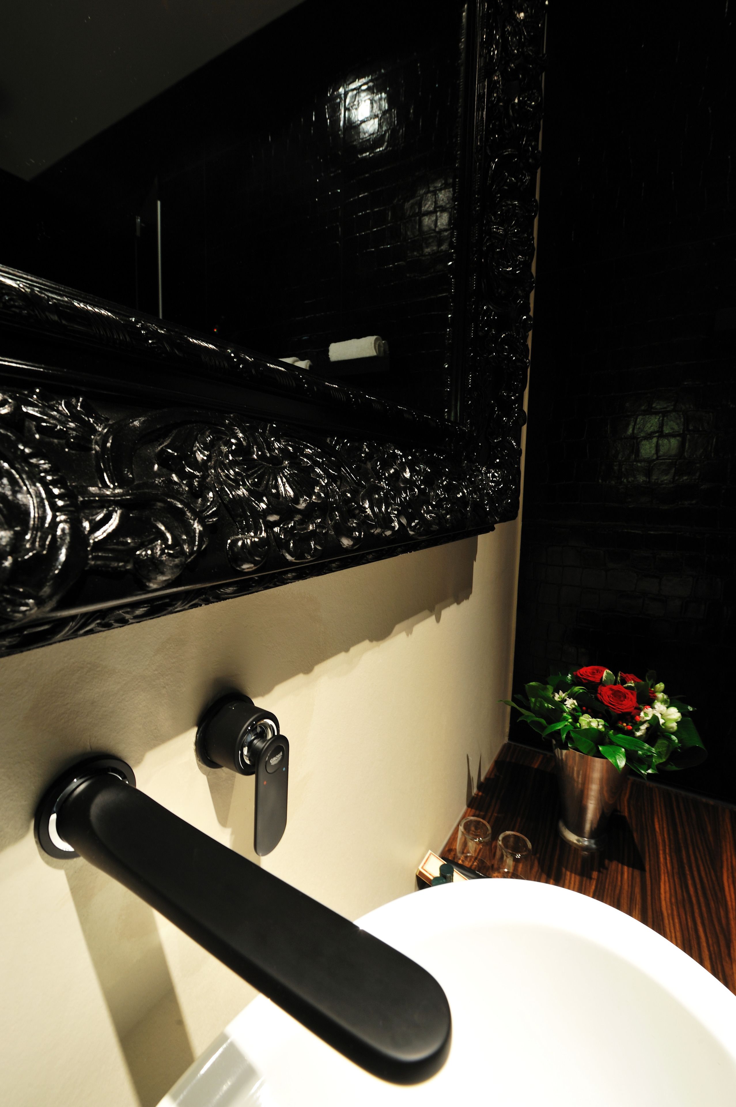 Une salle de bain avec un lavabo blanc, un robinet noir et un pare-éclaboussures noir décoratif.