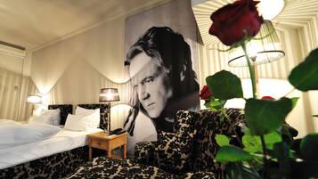 Une chambre d’hôtel avec un grand portrait accroché au mur, un lit recouvert de draps blancs, une table de chevet avec une lampe et un canapé à motifs léopard.