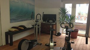 A home gym with exercise equipment, a television, a bench, and a large window. - Hotel Lessing (Düsseldorf)