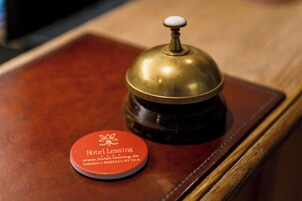 Una campana in ottone con pomello bianco su una superficie di legno, accanto a una tessera rossa dell'hotel con i recapiti.
