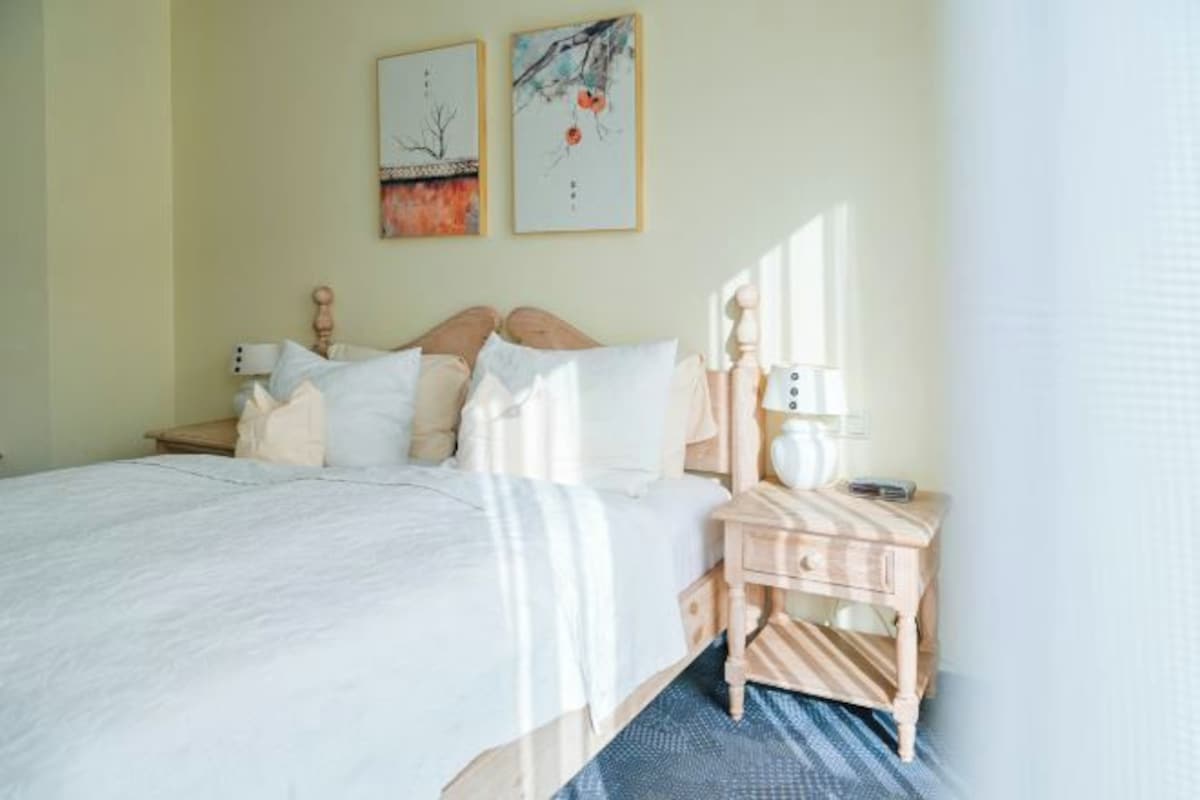 A neatly made bed with a wooden headboard, a bedside table with a lamp, and two framed artworks on the wall.