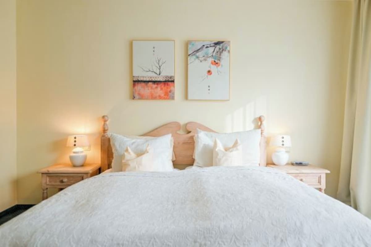 A neatly made bed with white bedding, two bedside tables with lamps, and two wall-mounted artworks.