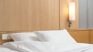 Ein ordentlich bezogenes Bett mit weißen Leinen und einer wandmontierten Lampe.