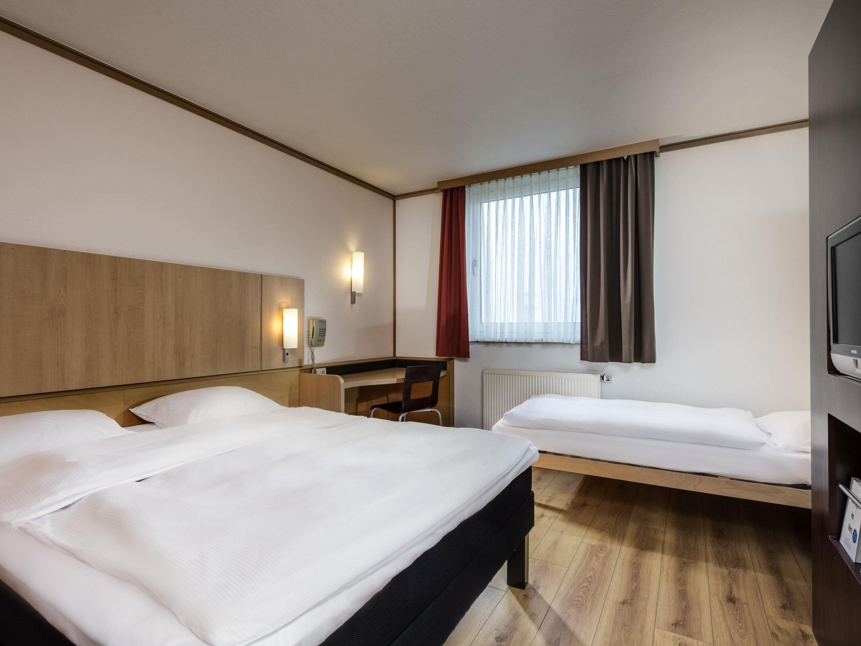 Habitación de hotel con dos camas, un escritorio, una silla, un televisor y una ventana con cortinas.