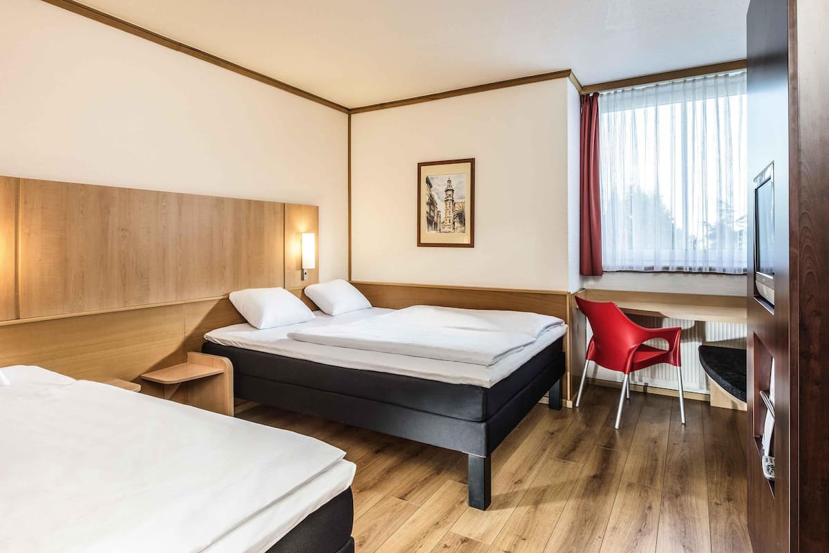 Une chambre d’hôtel avec deux lits, un bureau, une chaise, une télévision et une fenêtre avec des rideaux.