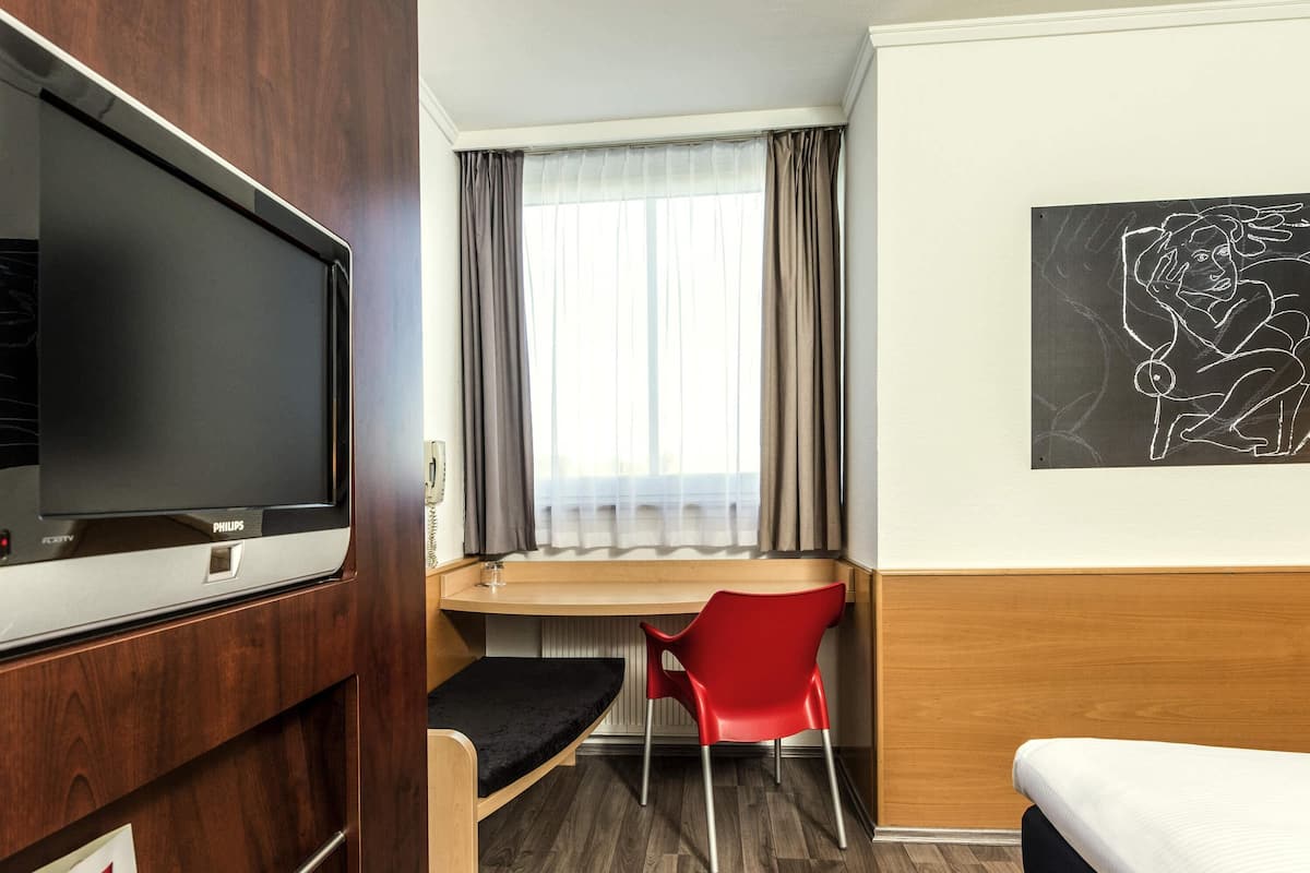 Une chambre d’hôtel équipée d’un lit, d’un bureau, d’une chaise, d’une télévision et d’une fenêtre avec des rideaux.