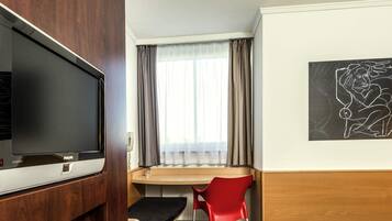 Une chambre d’hôtel équipée d’un lit, d’un bureau, d’une chaise, d’une télévision et d’une fenêtre avec des rideaux.