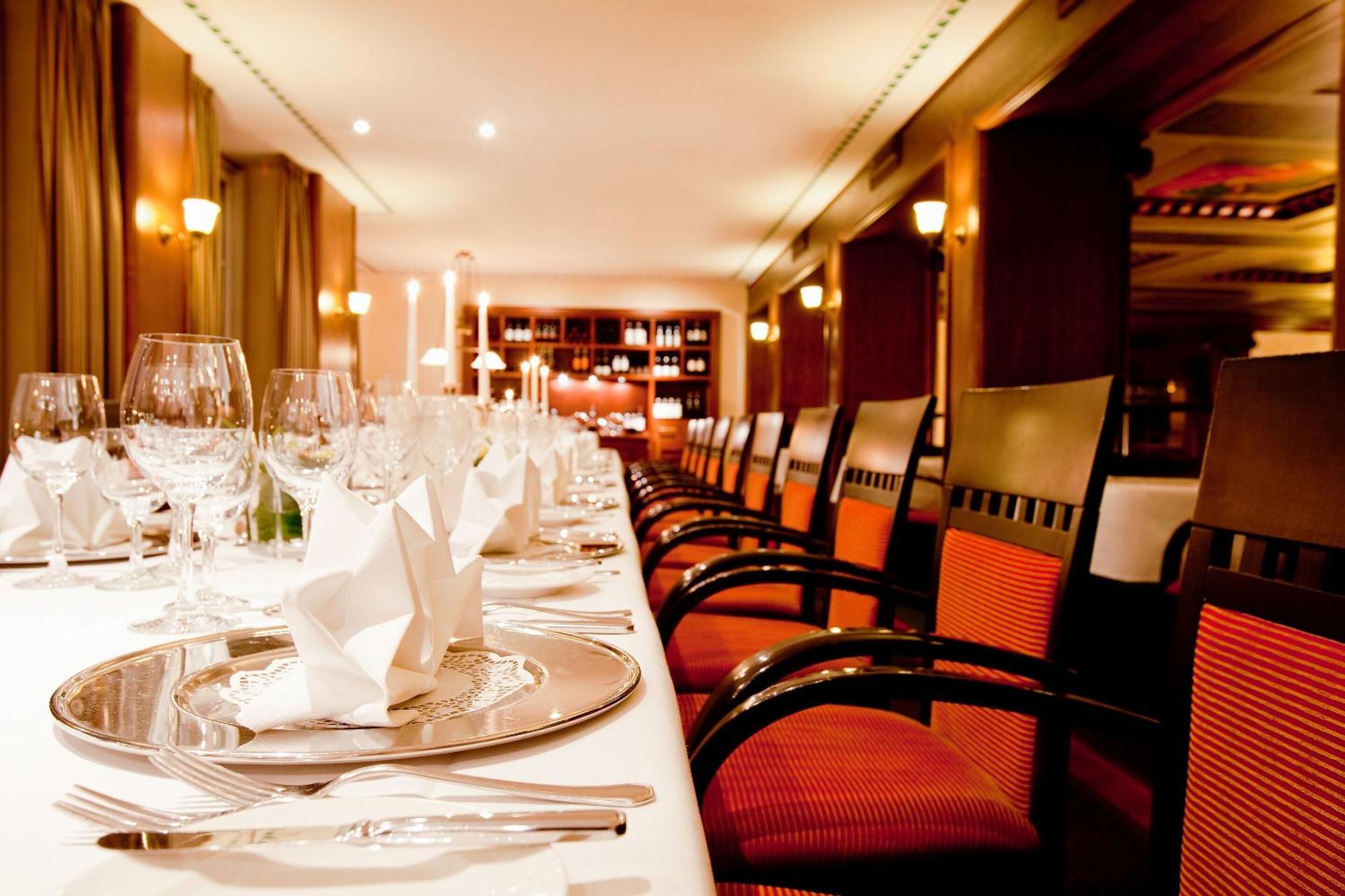 A long dining table set with multiple place settings, including plates, cutlery, and glasses.