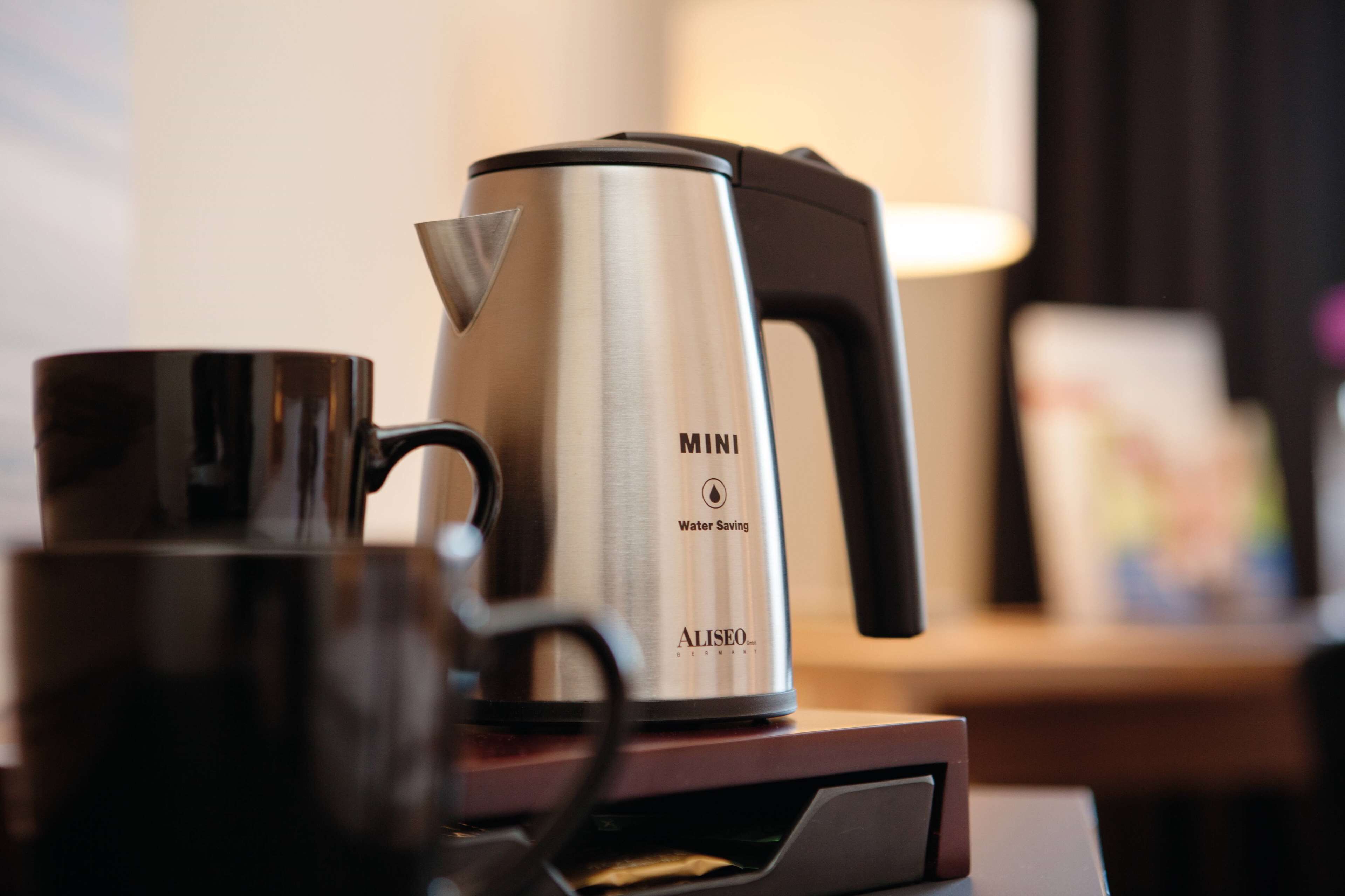 A stainless steel mini water-saving coffee maker on a table with a black mug.