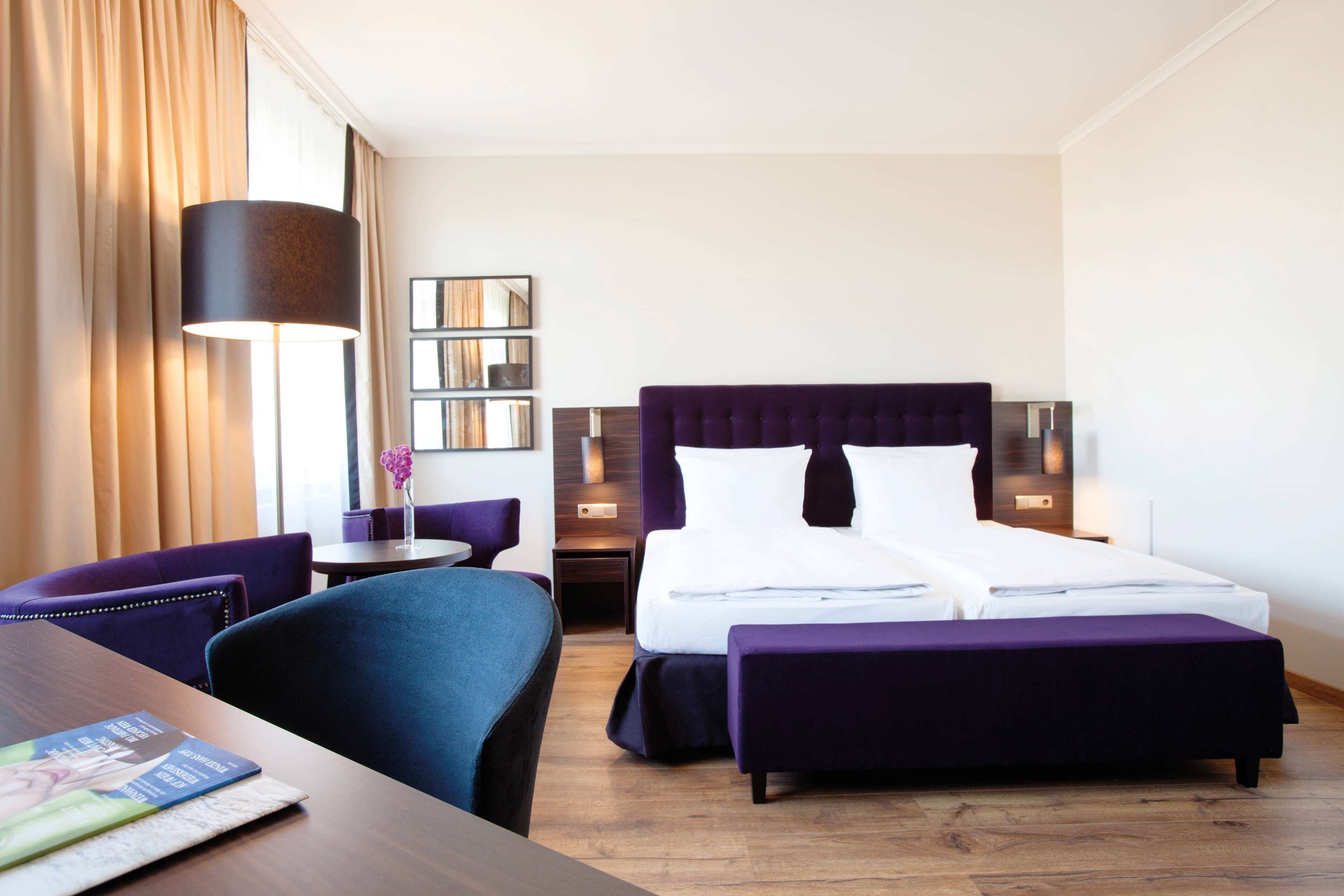 Habitación de hotel con una cama grande, un escritorio, una silla, una mesita y una lámpara.