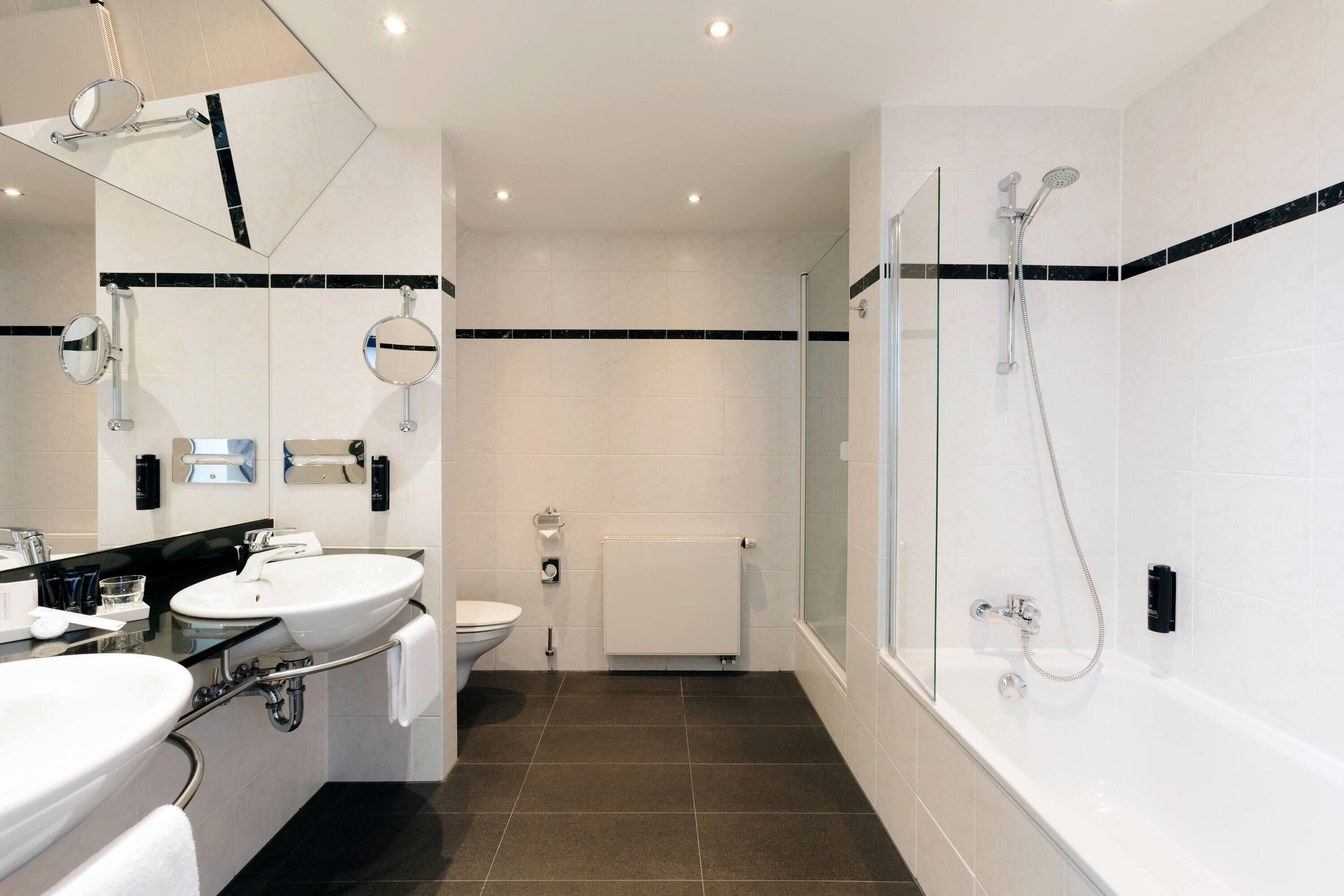 Un baño moderno con bañera, ducha, inodoro y dos lavamanos.