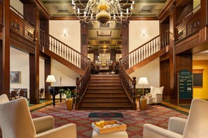 Eine prächtige Treppe führt zu einer zweiten Etage, gesäumt von hölzernen Geländern und einem Chandelier.