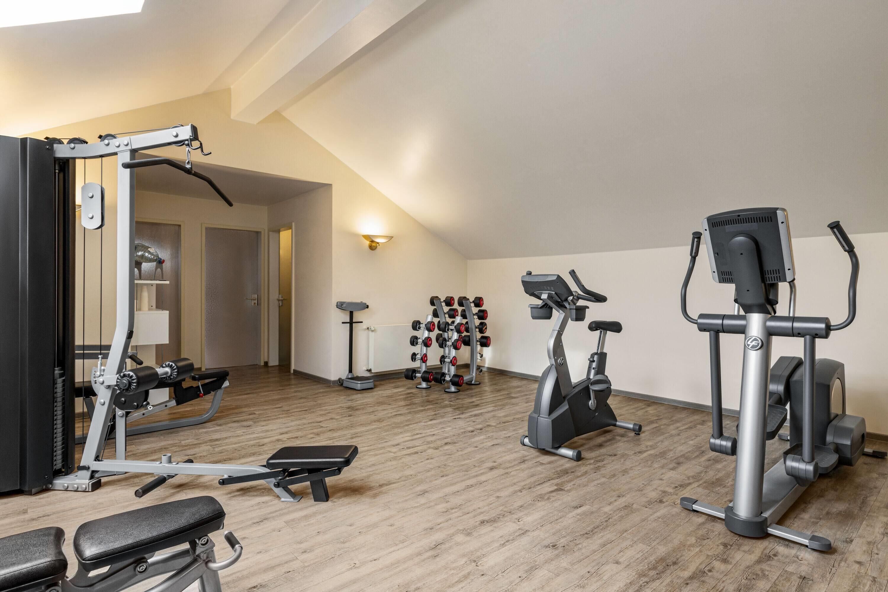 A home gym with a bench press, elliptical, and weight rack.