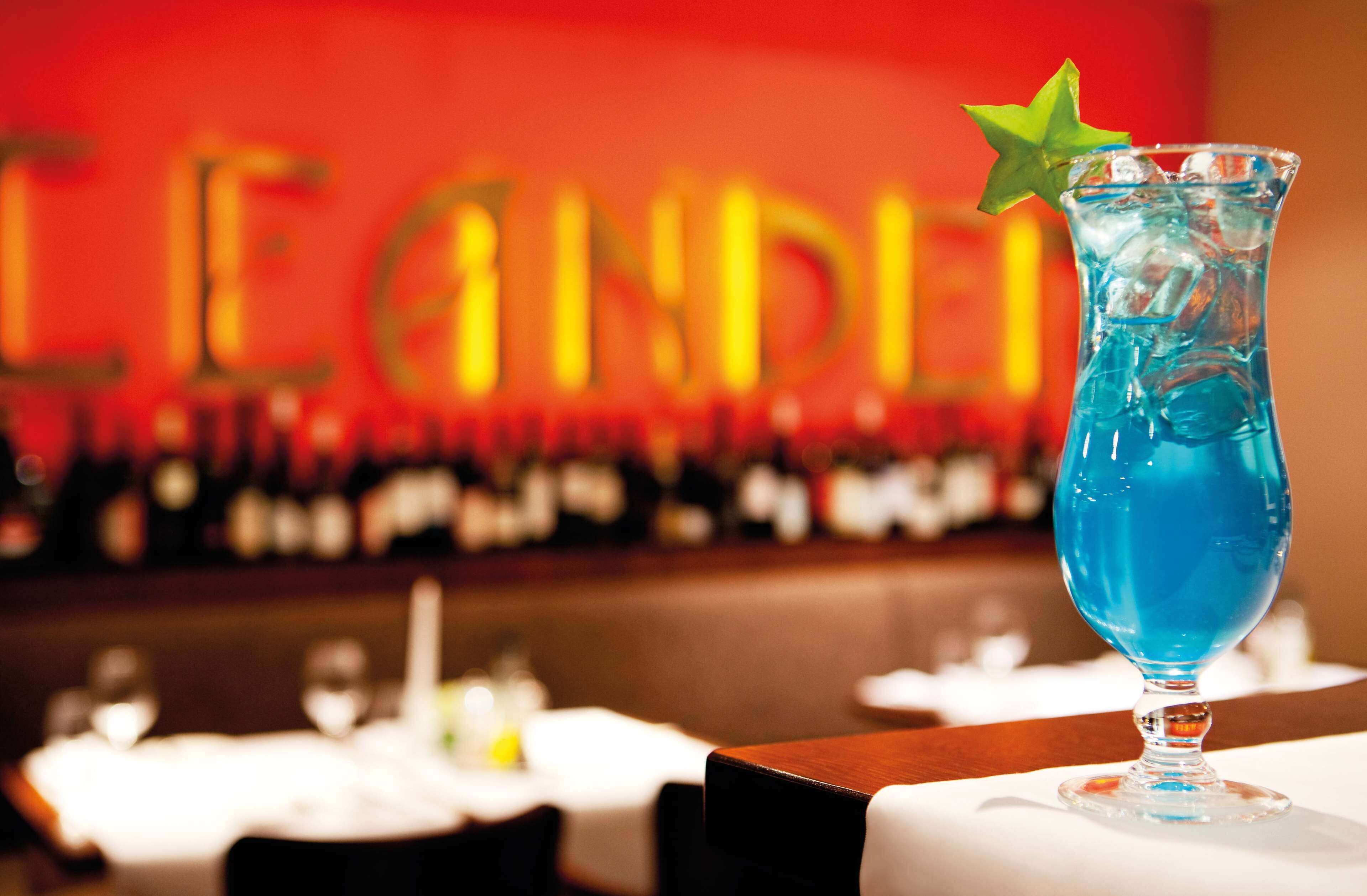 A bar setting with a blue cocktail in a glass with a star garnish, and a red wall with golden letters.