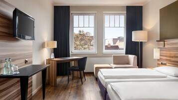 Habitación de hotel con escritorio, dos camas, televisor y ventana con cortinas.