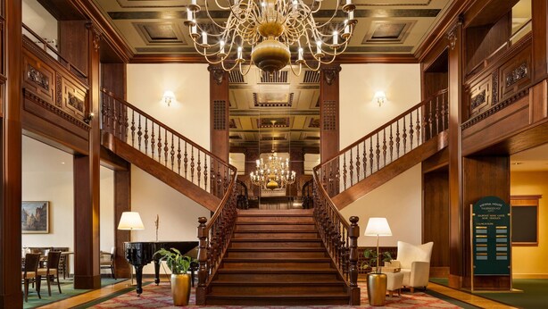 Un amplio vestíbulo con escaleras, candelabros y un piano.