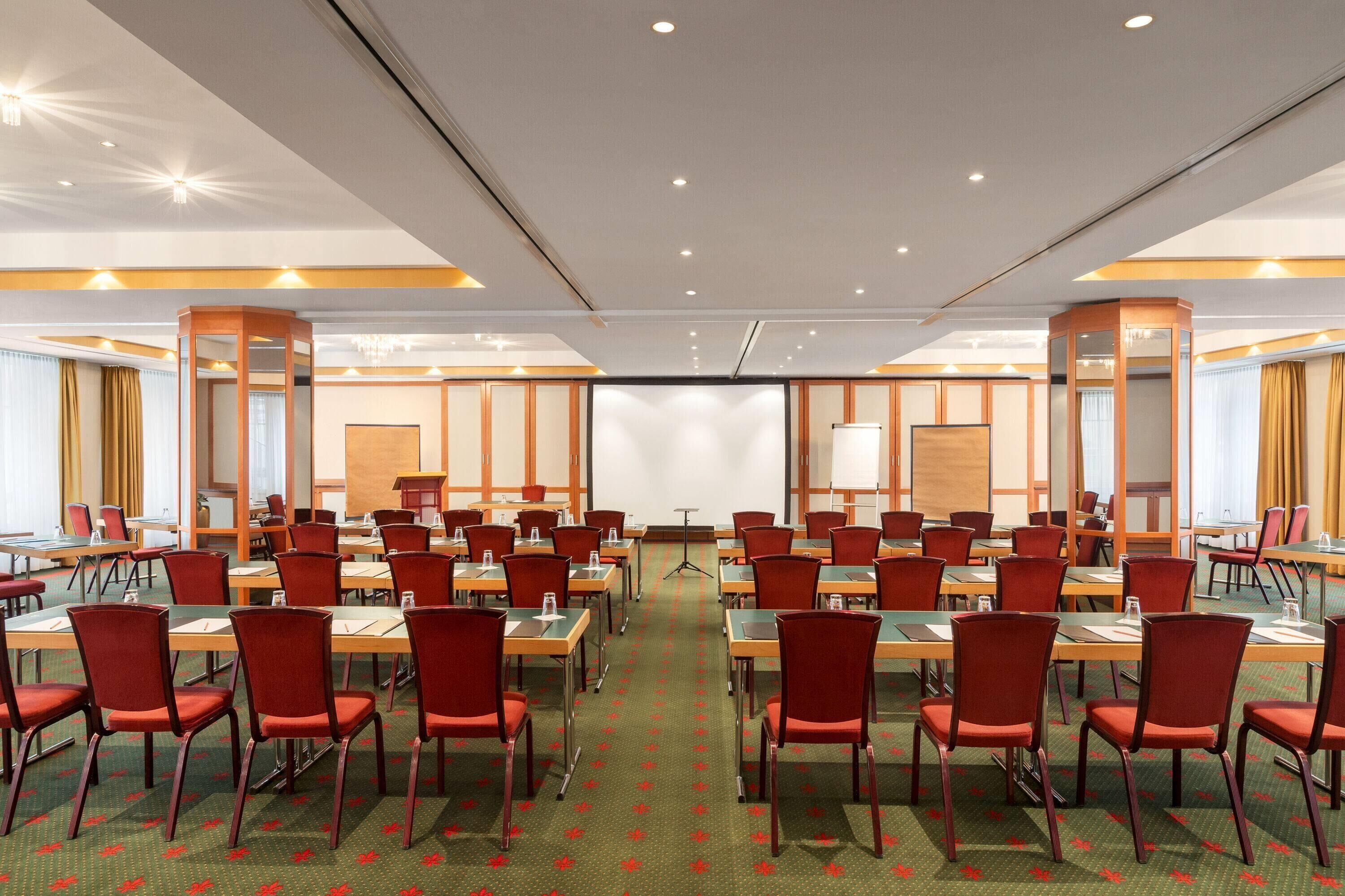 A conference room with multiple tables and chairs, a projector screen, and a presentation podium.